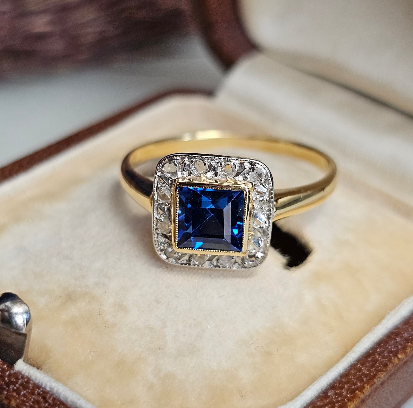 Bague ancienne Art Déco de forme carrée aux coins arrondis. Elle est sertie d'un Spinelle de synthèse bleu intense carré et taillé à degré, entouré d'un pavage de roses de diamant sur Or blanc. La monture est en or jaune 18 carats.