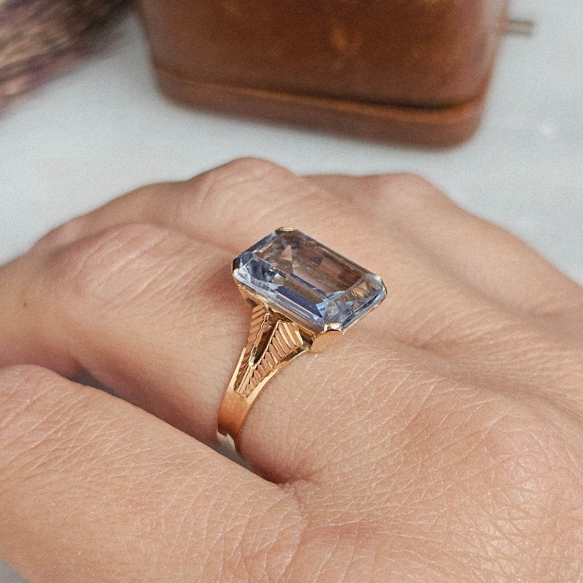 Bague cocktail vintage vers 1950 en or 18 carats et pierre bleue rectangulaire de type spinelle. La monture présente un dessin ajouré et strié, vue portée