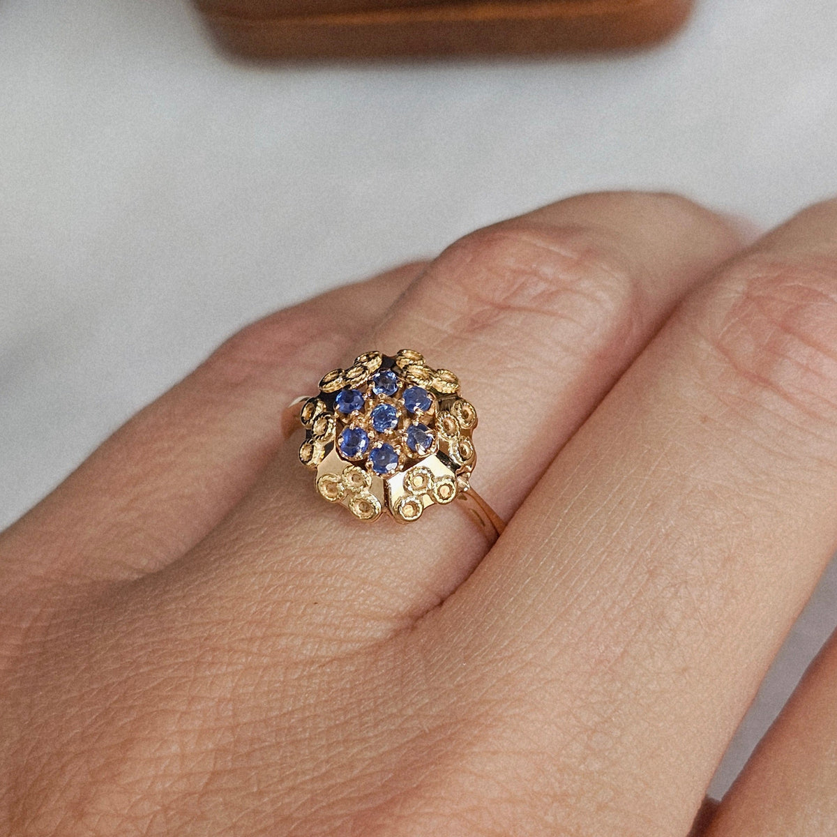 Bague fleur ancienne vers 1950, en or jaune et rose, sertie de saphirs et ornée d'un décor de petits cercles tressés, vue portée