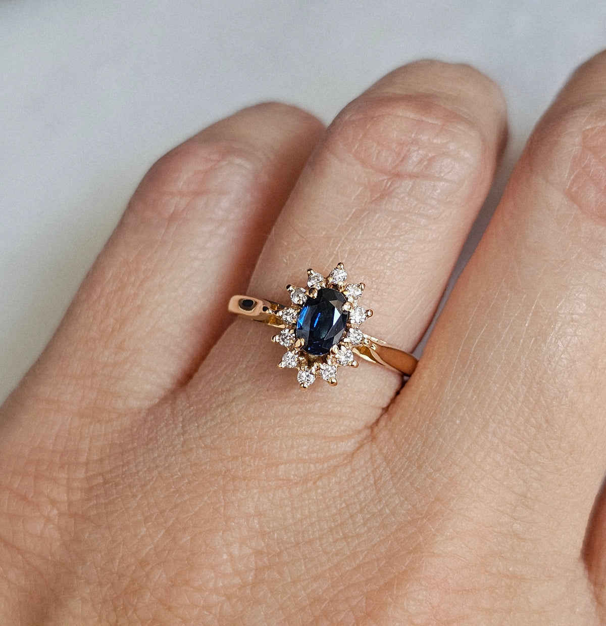 Bague de fiançailles type marguerite, avec saphir et diamants, sur une monture en or jaune 18 carats, vue portée
