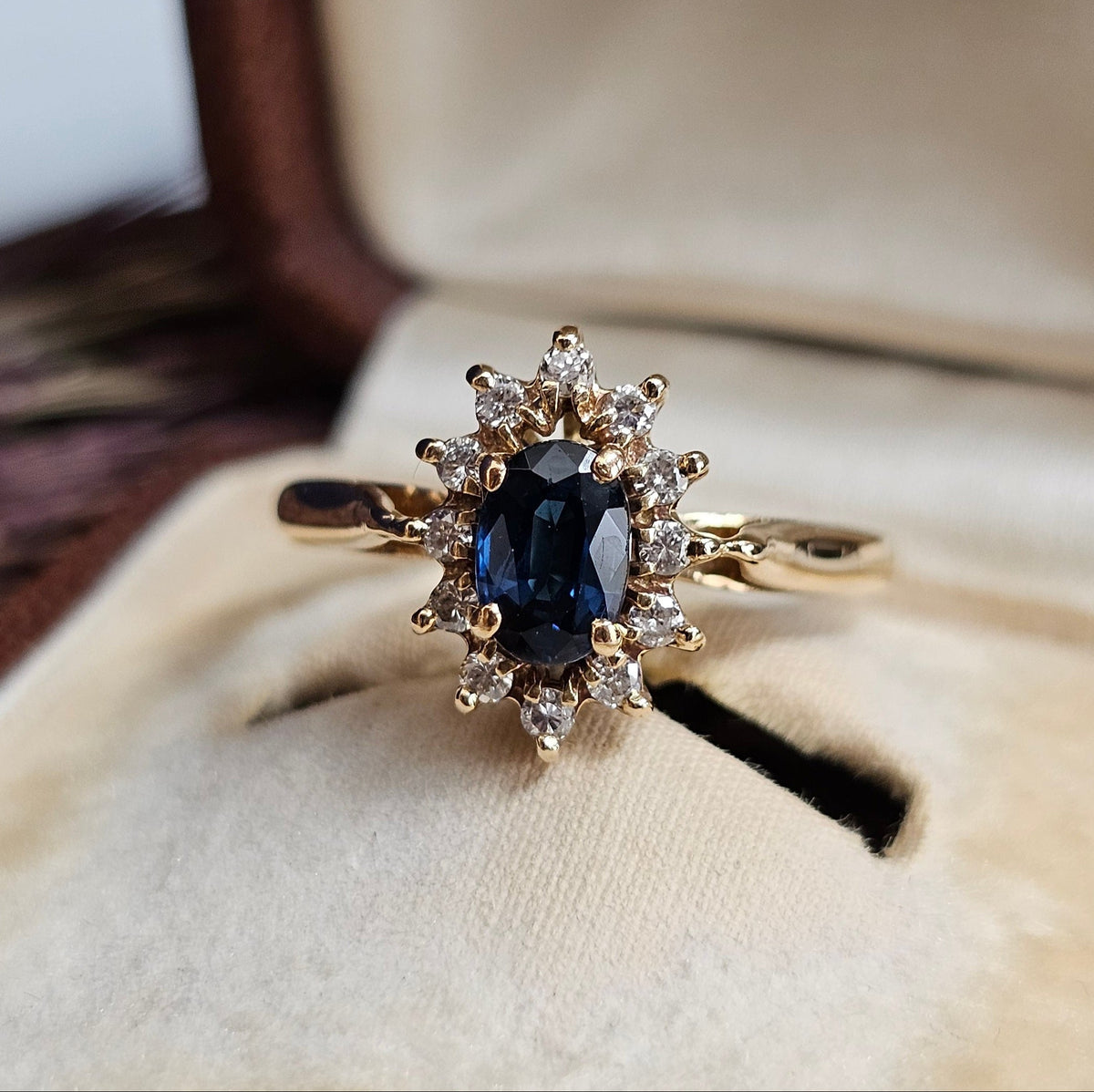 Bague de fiançailles type marguerite, avec saphir et diamants, sur une monture en or jaune 18 carats.