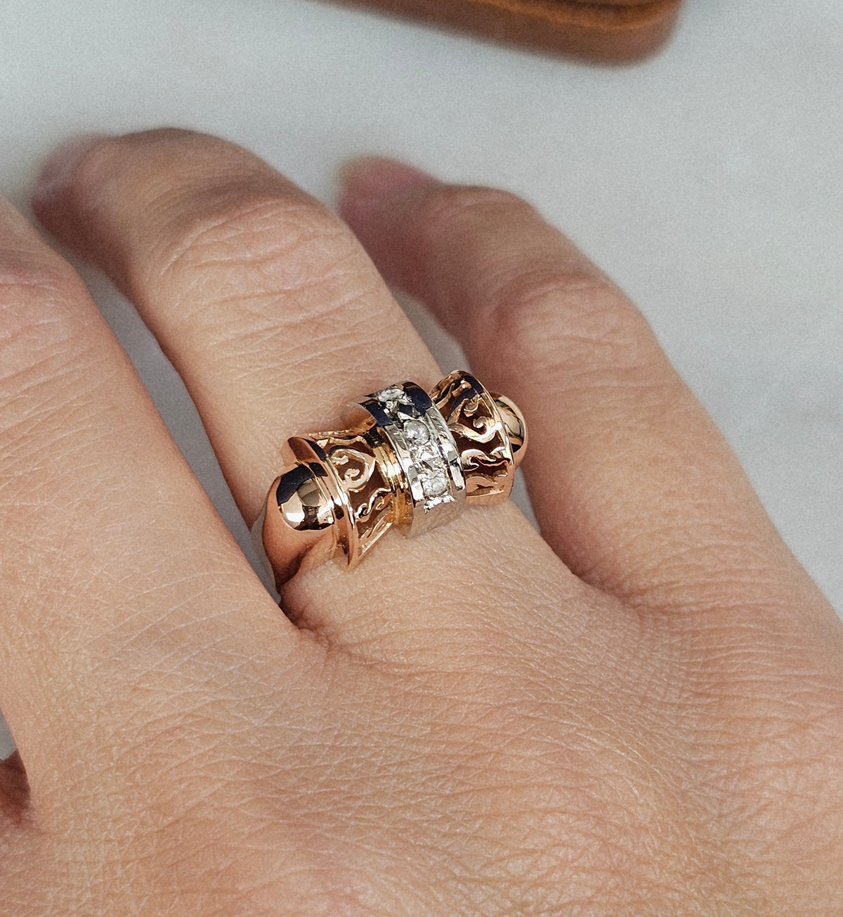 Bague ancienne vers 1940 en forme de noeud stylisé, en or rose et blanc, sertie de trois pierres blanches, vue portée